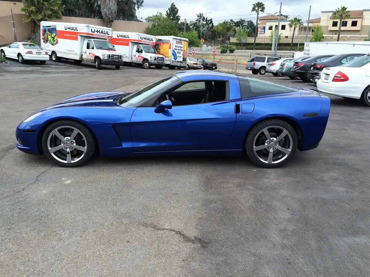 The same blue Chevrolet Corvette rebuilt and back together outside the shop, panels aligned and the paint finished, parked in the lot on West Bradley Avenue